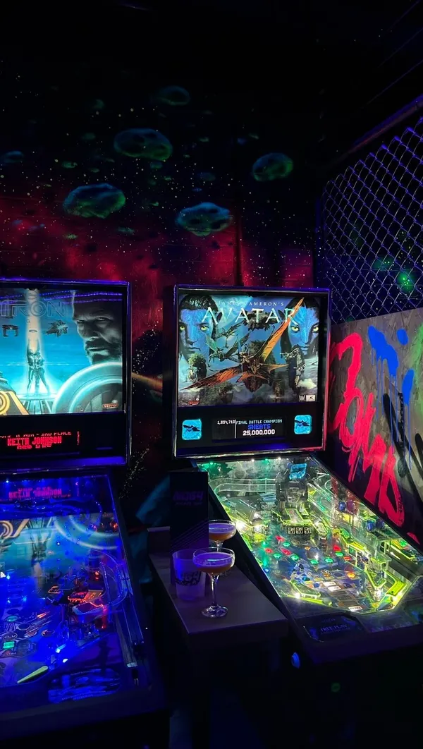 This video showcases NQ64, a retro arcade bar in London. It features various cocktails (including one prepared with a flambé), gameplay on Star Wars pinball and other arcade games, and the bar's atmosphere. The video highlights the bar's 80s aesthetic and emphasizes the fun, social aspect of the experience.