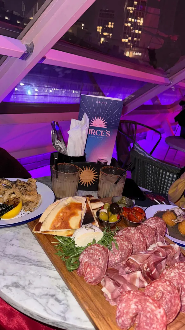 This video showcases a visit to Circe's Rooftop bar and restaurant. The video begins with an exterior shot of the venue at night, followed by interior shots of the decor, including neon lights and straw decorations. The video highlights the food and drinks ordered, including a charcuterie board, mozzarella and truffle arancini, nori dusted calamari, and spicy margaritas. The presentation of the food is emphasized with close-up shots. The video also features a photo booth experience with friends. The main focus is on showcasing the restaurant's ambiance, food, and overall experience.