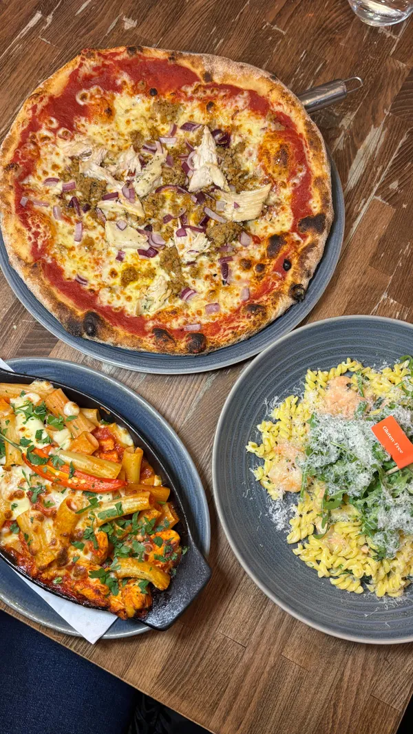 A promotional video for the Italian restaurant chain, Prezzo. The video showcases a variety of dishes, including a rigatoni arrabbiata al forno with a prominent cheese pull, a sharing board with cured meats and olives, a Tuscan BBQ chicken pizza, and several gluten-free options like a creamy king prawn & salmon fusilli and a tomato bruschetta. The video also features shots of the restaurant's exterior, interior, and a dedicated gluten-free menu, highlighting its suitability for diners with dietary restrictions.
