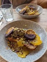 A high-quality, well-lit food photograph of a Panettone French toast dish served at a cafe. The image captures the texture and vibrant colors of the food, utilizing a shallow depth of field to focus on the main dish while providing context with a secondary plate in the background.