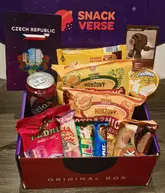 A straightforward, functional product shot of a 'Snackverse' subscription box featuring various Czech snacks, including crisps, gummies, and a drink. The image is taken from a high angle, showing the contents of the box against its branded packaging.