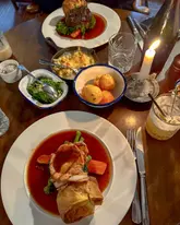 A top-down, atmospheric shot of a Sunday roast spread at a pub, featuring plates of roast beef with gravy, cauliflower cheese, peas, and roast potatoes, illuminated by a candle.
