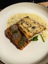 A high-quality, close-up shot of a seared halibut dish served with a crispy potato terrine, spinach, and a champagne beurre blanc sauce. The plating is precise and elegant, showcasing the culinary skill of the venue.