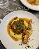 A high-quality, top-down shot of a slow-braised ox cheek dish served with mashed potatoes and a roasted carrot, presented in a restaurant setting.