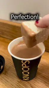 A short, first-person POV video showcasing a visit to Knoops. It begins by panning across the menu wall displaying various chocolate percentages and finishes with a close-up shot of a hot chocolate being stirred and a marshmallow being dipped into the drink.