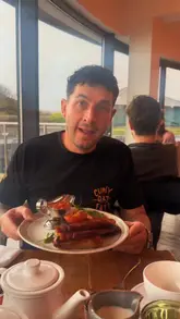 A creator reviews a Full English breakfast at Gara Rock Hotel, highlighting the quality of ingredients like maple bacon and black pudding. The video features the creator talking to the camera with close-up shots of the plated food.