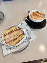 A top-down, flat-lay photograph of a pastrami bagel and a chai latte served on a metal tray at a cafe.