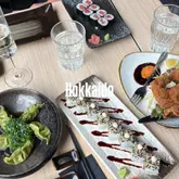 An overhead flat-lay shot of a Japanese lunch spread featuring sushi rolls, dumplings topped with seaweed salad, and a fried dish, set on a light wood table.
