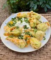 A top-down, close-up shot of deep-fried courgette flowers stuffed with ricotta and herbs, served on a white plate with a dollop of yogurt and garnished with fresh mint.
