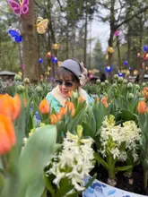 A high-quality, well-composed portrait of a visitor at a tulip festival. The image uses a shallow depth of field to isolate the subject against a vibrant, colourful background of flowers, creating an inviting and aspirational atmosphere for a day out.