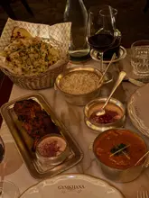 A high-quality, atmospheric overhead shot of a spread at a high-end Indian restaurant, featuring lamb chops, curry, naan, and rice. The lighting is warm and moody, perfectly capturing the upscale dining experience.