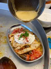 A close-up shot capturing the moment butter is drizzled over a plate of Yogurtlu Tantuni, highlighting the textures of the yogurt, meat, and bread.