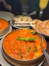 A top-down, flat-lay style photograph of an Indian meal featuring a central curry dish, rice, and naan bread, captured in a restaurant setting.