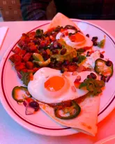 A close-up, 45-degree angle shot of a plate of Huevos Rancheros topped with chorizo. The dish is clearly presented, but the image is heavily impacted by a strong, unnatural red lighting cast that distorts the natural colours of the food.