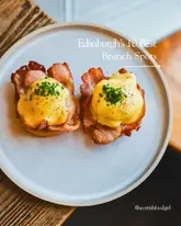 A high-quality, top-down shot of two eggs benedict dishes on a plate, used as a cover image for a listicle about brunch spots in Edinburgh.