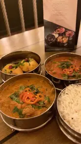 A promotional video showcasing the 'Lite Tiffin' menu at Mowgli Street Food. The video features close-up shots of the tiffin tins, various curries, rice, and chat bombs, interspersed with shots of the restaurant's distinctive interior decor, including swings and fairy lights, and an exterior shot of the venue.