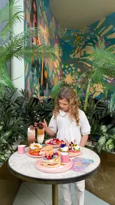A montage of brunch dishes and specialty drinks at a cafe, featuring teddy bear-topped hot chocolates, iced coffees, pancakes, and savoury brunch plates.