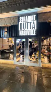 A fast-paced, music-synced video showcasing a visit to 'Straight Outta Nashville' in Burnley. The video features quick cuts of the venue's interior, the ordering kiosk, and a variety of indulgent food items including a large 'munch box' containing burgers, fries, and chicken, as well as a cheesecake dessert. The creator demonstrates the food with close-ups of cheese sauce being poured and chicken being dipped.