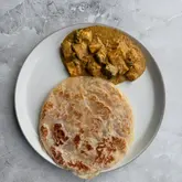 A simple, overhead shot of a plate containing a paratha and a serving of paneer butter masala on a grey marble surface.