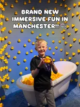 A photo of a child holding a rubber duck in front of a wall of rubber ducks at the Bubble Planet Experience in Manchester.