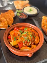 A close-up, high-angle shot of a Turkish lamb shank served in a clay pot, surrounded by side dishes including pide and dips, presented on a dark table.