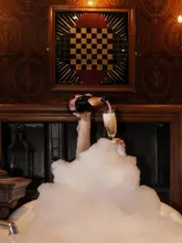 A highly atmospheric and luxurious shot taken at The Witchery in Edinburgh, featuring a hand pouring champagne into a glass amidst a bubble bath, set against a dramatic, ornate fireplace backdrop.
