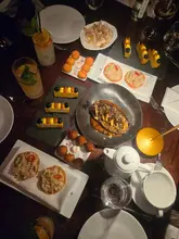 An overhead shot of a table filled with various Spanish tapas dishes, including crab tostadas, patatas bravas, and aubergine, captured in a dimly lit restaurant setting using direct flash.
