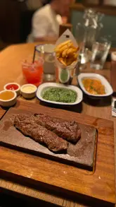 A couple visits Flat Iron restaurant, showcasing the menu, cocktails, various steak dishes, sides, and the complimentary soft-serve ice cream experience using a branded knife coin.