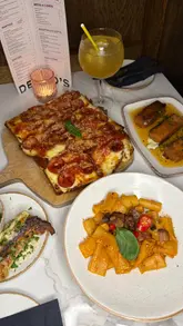 A video review of Deano's in Manchester, featuring a variety of Italian-American dishes including mozzarella sticks, deep-dish focaccia pizza, rigatoni alla vodka, and garlic twists. The creator provides commentary on the taste and texture of the food while showcasing the restaurant's moody atmosphere.