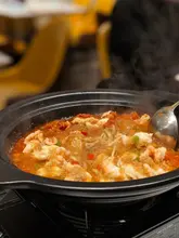 A close-up, eye-level shot of a steaming pot of prawn vermicelli being served with a ladle, set against a blurred restaurant background.