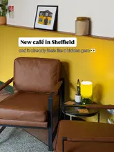 A cozy, well-lit interior shot of a cafe featuring brown leather armchairs and a yellow accent wall, designed to evoke a comfortable, living-room-style atmosphere.