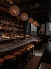 A high-quality, atmospheric interior shot of a sophisticated hotel bar, likely The Nomad, showcasing the moody lighting, marble bar top, and classic bar design. The image captures the upscale, historic ambiance of the venue.
