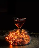 A highly stylized, editorial-quality photograph of a cocktail served in a coupe glass, surrounded by a dramatic, glowing pyrotechnic effect against a pitch-black background. The image emphasizes luxury and atmosphere, suitable for high-end hospitality marketing.