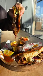 A fast-paced food review video featuring a visit to a Manchester-based street food vendor. The creator showcases their signature birria taco ramen, birria tacos, loaded fries, and churros. The video uses quick cuts, voiceover commentary, and close-up shots to highlight the texture and quality of the food, particularly the cheese pulls and rich broth.