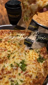 A short promotional video for Paratha Box in Edinburgh, featuring close-ups of their menu items including a cheese-heavy paratha pizza, a kebab paratha roll, mango lassi, and karak chai, alongside shots of the restaurant's interior.