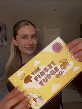 A creator holds up an Easter-themed box of fudge from 'The Finest Fudge Co.' in a selfie-style shot. The image is clear and well-composed for social media, focusing on the product packaging.