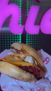A fast-paced, energetic promotional video featuring a creator trying new breakfast items at Archie's. The video highlights the venue's signature pink and neon aesthetic while showcasing various breakfast burgers, hash browns, waffles, and shakes.