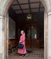 A woman walks through a grand stone archway into the wood-paneled interior of Bovey Castle, capturing a sense of timeless elegance and luxury.