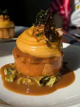 A high-quality, close-up shot of a Hereford beef pie served with smooth mash, braised greens, and a rich gravy, captured in natural sunlight at a village pub.