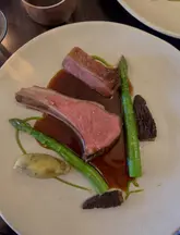 A close-up, high-quality shot of a plated lamb dish featuring asparagus and morels, presented with a refined sauce drizzle, indicative of a fine dining spring menu.