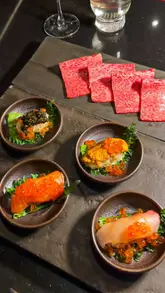 A high-quality, polished reel showcasing a Japanese A5 Wagyu yakiniku tasting menu at a London restaurant. The video features close-up shots of raw and grilled meats, sushi, and cocktails, emphasizing the premium nature of the ingredients and the interactive dining experience.