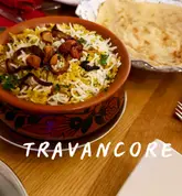 A close-up, slightly elevated shot of a bowl of chicken biryani served with a side of paratha on a wooden table, with the restaurant name overlaid in white text.