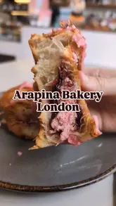 A short, visual-focused reel showcasing two pastries—a raspberry scroll and a cookie croissant—being pulled apart and cut, alongside an iced coffee, at a bakery.