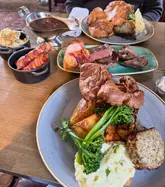 A high-angle, appetizing shot of a generous Sunday roast spread, featuring multiple plates of meat, vegetables, and gravy, capturing the essence of a hearty pub meal.