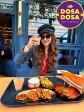 A vibrant, well-composed shot featuring a diner enjoying a South Indian feast at Dosa Dosa. The image captures a variety of dishes including dosa, curry, and street-style snacks, presented in a welcoming, casual restaurant setting.