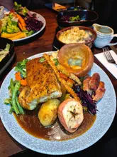 A high-angle, close-up shot of a Sunday roast dinner featuring pork belly, a Yorkshire pudding, roast potatoes, and various sides, served in a restaurant setting.