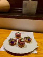 A close-up, high-quality shot of four intricate, fine-dining appetizers served on a white plate, showcasing precise plating and high-end ingredients.