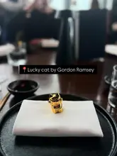 A clean, minimalist shot featuring a golden lucky cat figurine placed on a crisp white napkin at a table setting, with a blurred restaurant interior in the background.