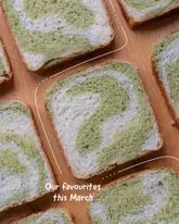 A clean, overhead flat-lay photograph of several slices of green and white marble milk bread arranged on a wooden surface. The image features a simple white line graphic overlay and text, presenting the bread as a monthly favourite.