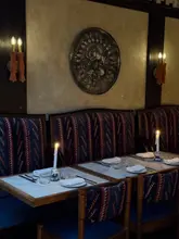A moody, atmospheric interior shot of a restaurant, featuring candlelit tables and patterned upholstery, creating an intimate and upscale dining environment.